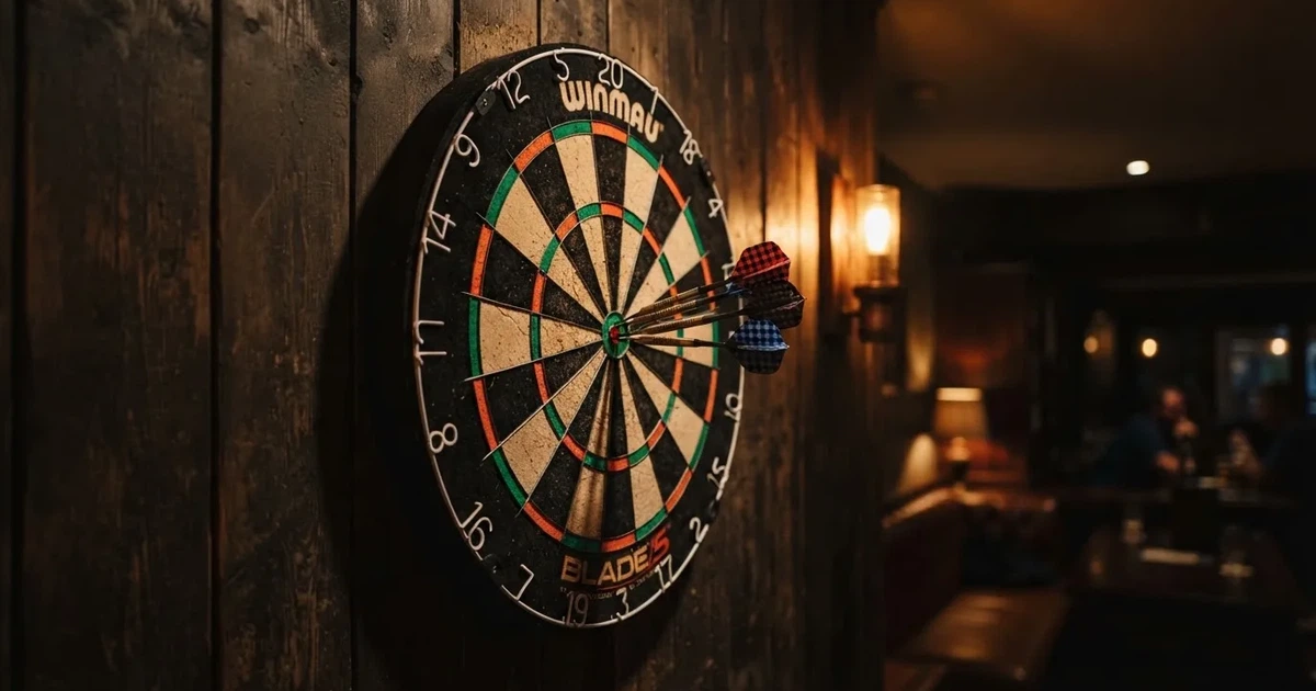 Eine Dartscheibe an einer Holzwand in einem schwach beleuchteten Raum, drei Pfeile stecken nahe der Mitte, warmes Licht von der Seite.